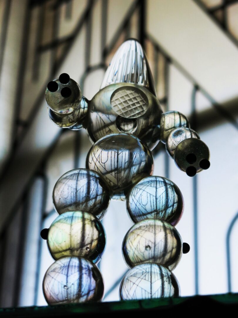 Transparent spheres stacked in a pyramid with metal details against a blurred window background.