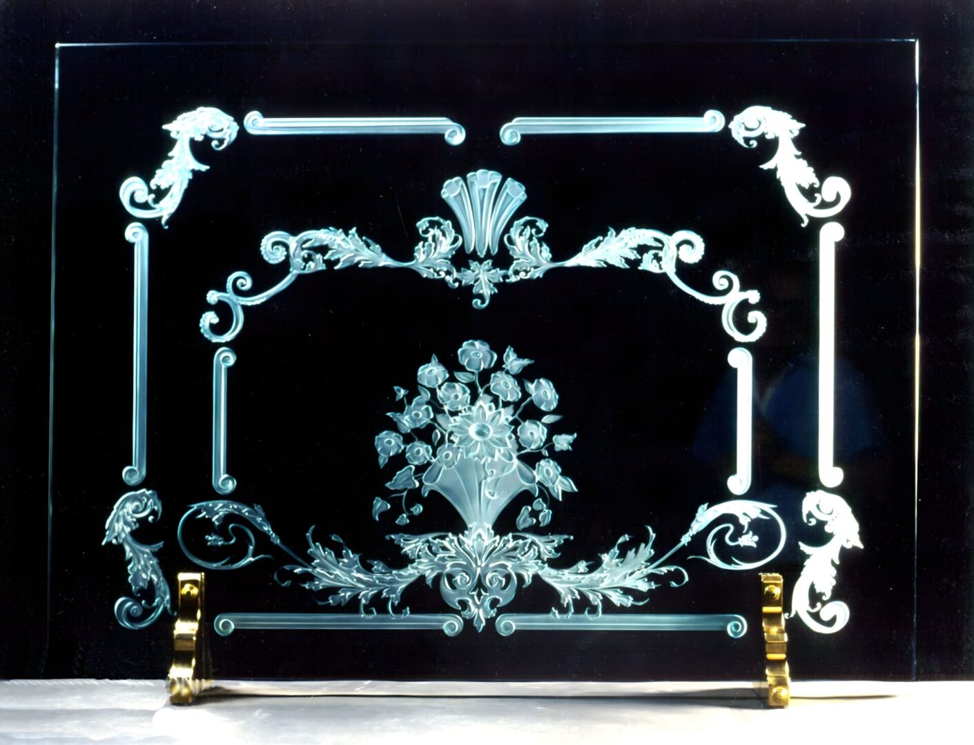 Ornate glass fireplace screen with white etched floral and scroll designs on a black background.