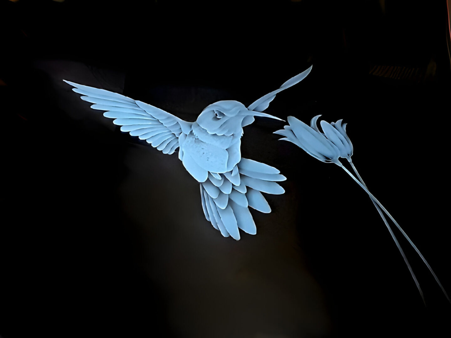 A paper art installation featuring a blue bird in flight approaching a flower, displayed against a dark background.