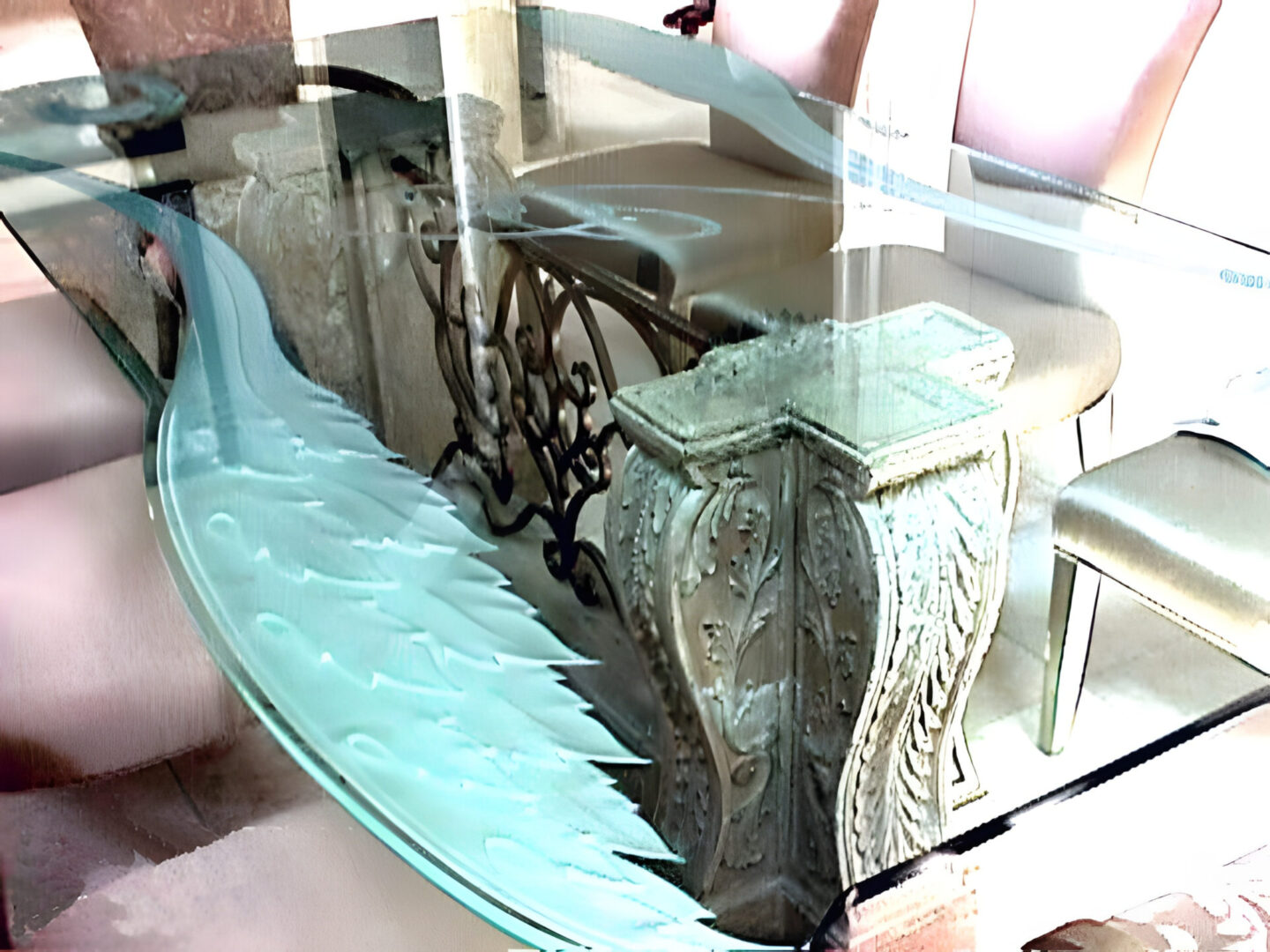 An ornately carved table base supporting a glass tabletop in a room with chairs and a reflection visible on the surface.