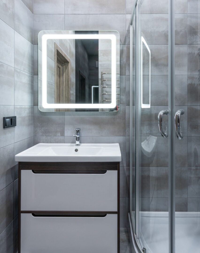 Modern bathroom with illuminated mirror and glass shower enclosure.