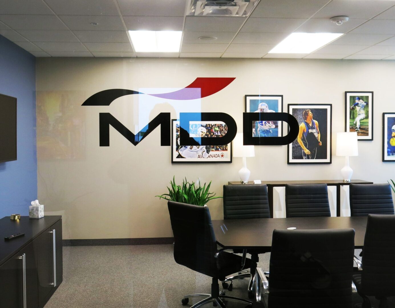 An office waiting area with a company logo on a glass partition, decorated with framed photographs on the wall.