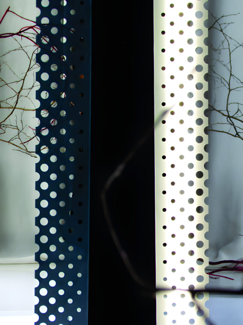A vertical composition showing contrasting panels with perforations near a window, featuring a glimpse of branches.
