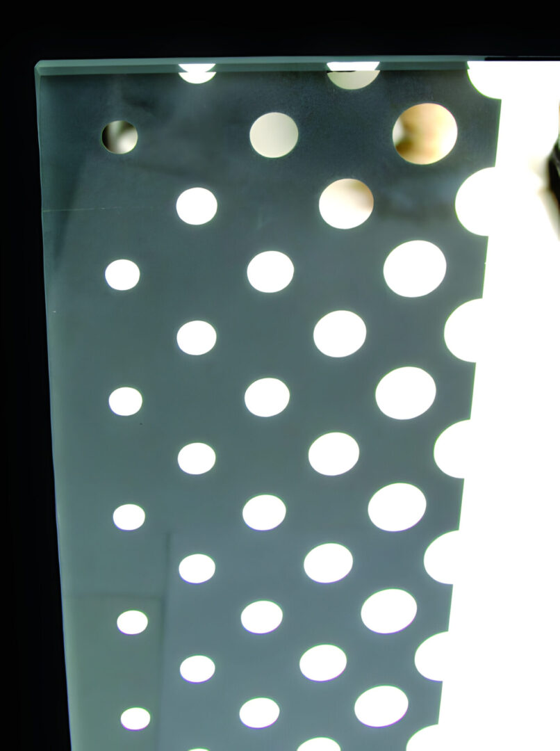 A metallic panel with perforations lit from behind creating a pattern of illuminated circles.