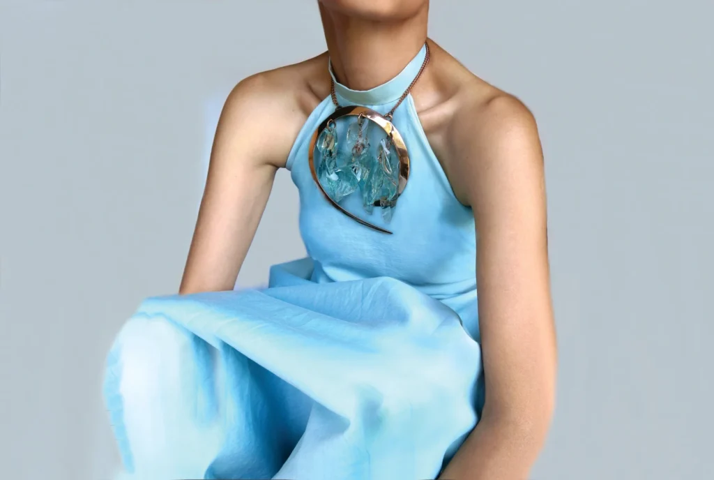 Woman in a blue dress with a large, circular metallic necklace.