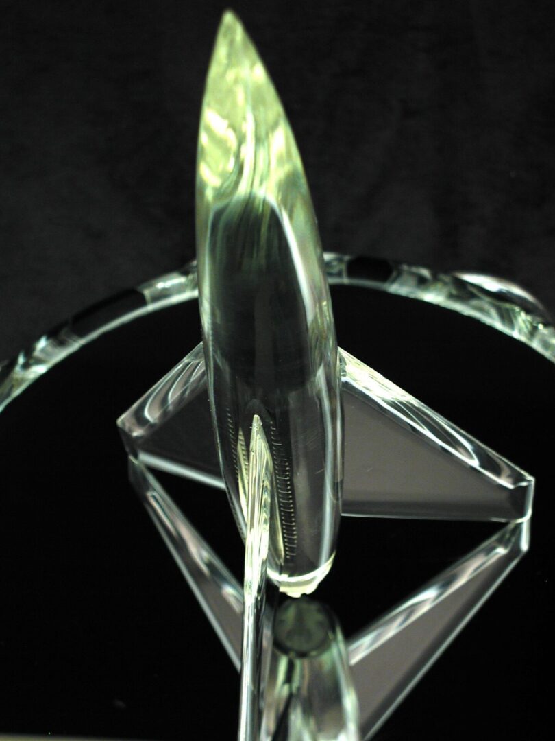 Clear glass sculpture with symmetrical design on a reflective surface.