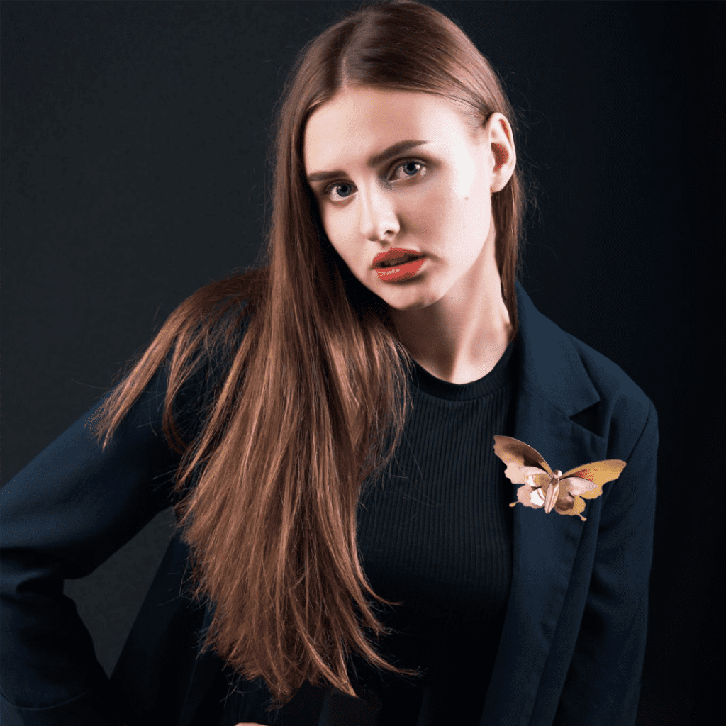 Woman with long hair posing in a black blazer, featuring a butterfly on her shoulder.