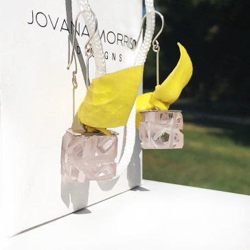 A pair of translucent cube earrings with yellow fabric accents displayed beside a branded backing card.