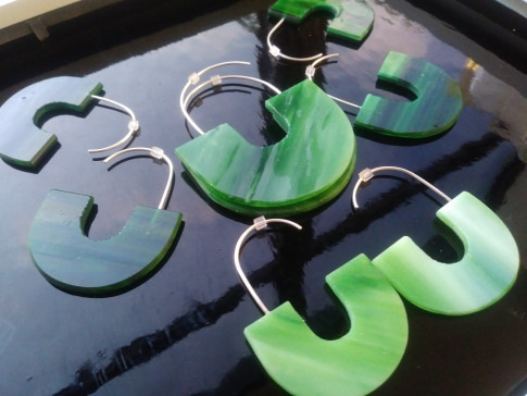 Five green, semi-transparent earrings shaped like the recycle symbol displayed on a reflective surface.