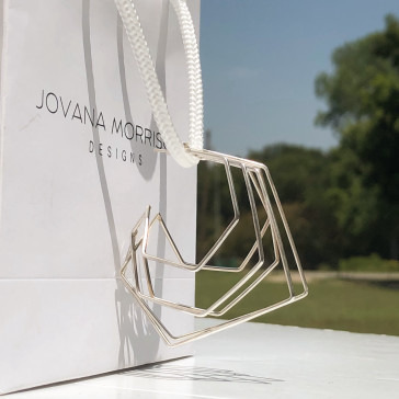 A geometric metallic purse beside a shopping bag with "jovana morris designs" printed on it.