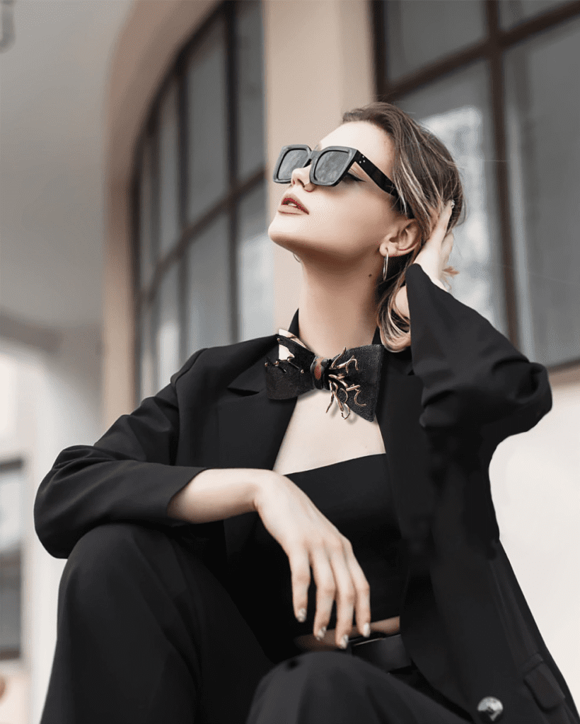 A woman in stylish black attire and sunglasses posing elegantly.