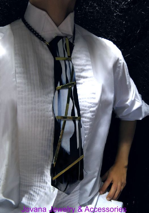 A mannequin wearing a white shirt and patterned tie with a dark background, displaying jewelry and accessories.