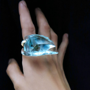 A large blue gemstone rests on a hand against a black background.