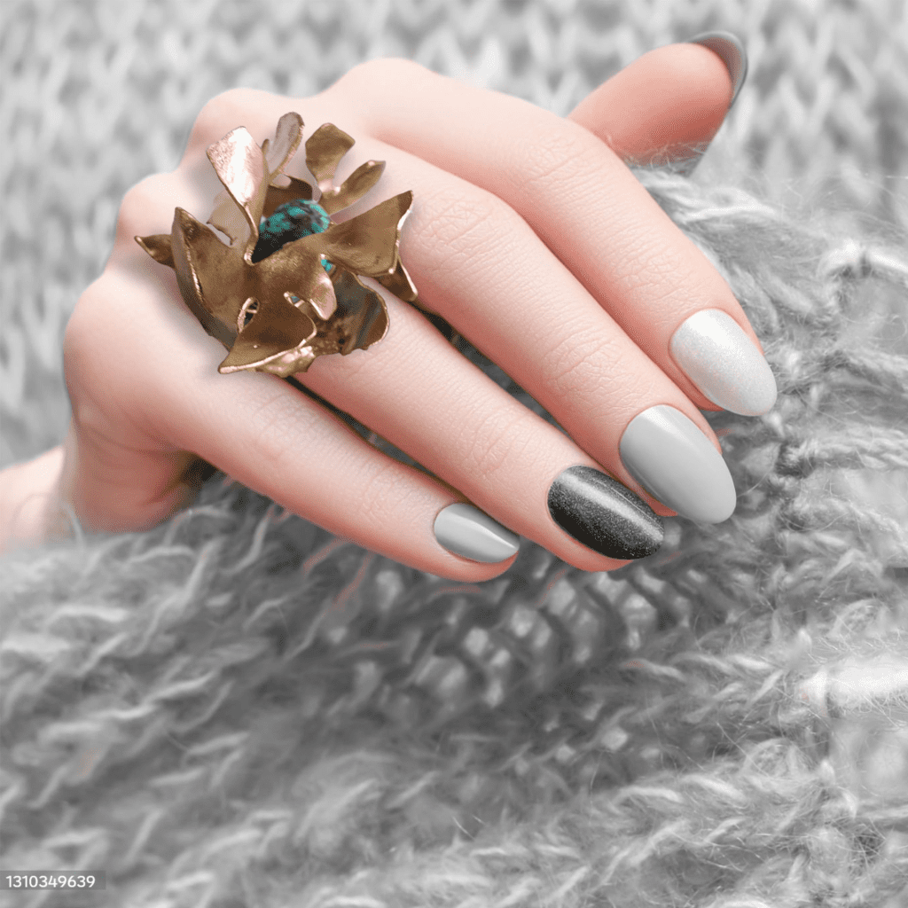 A hand with gray and black nail polish showcasing a large bronze ring with a blue gemstone, resting on a textured gray fabric.