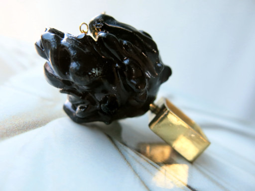 A close-up image of a black carved pendant with a gold clasp lying on a light fabric surface.