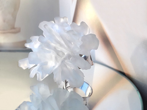 Translucent white artificial flower on a reflective surface with soft lighting.