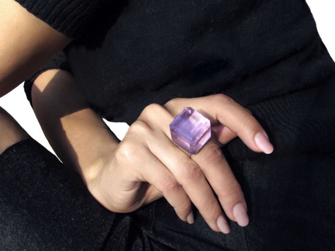 A person wearing a black sweater displaying a large purple gemstone rested on their intertwined fingers.