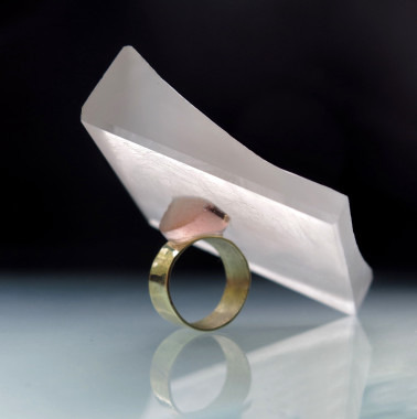 A ring positioned under a folded piece of paper on a reflective surface.