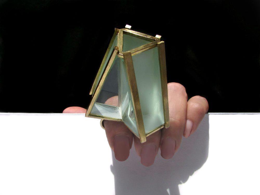 A hand holding a small geometric glass terrarium against a black and white background.