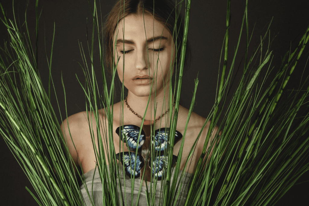 Woman meditating behind tall green grass with a butterfly on her necklace.