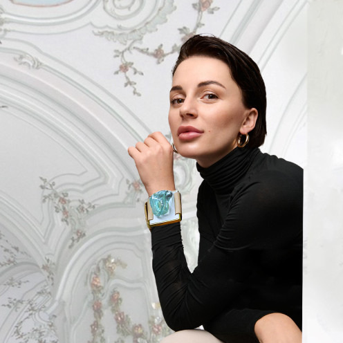 Woman with a stylish watch poses against an ornate backdrop.
