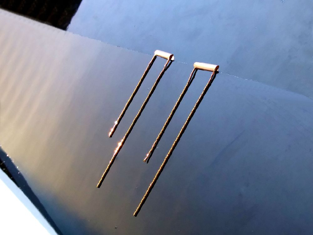 Three bobby pins lying on a reflective surface.