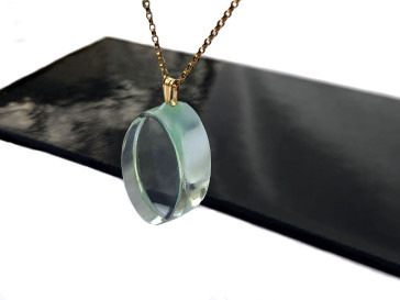 Transparent pendant on a gold chain lying on a reflective black surface.