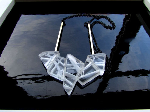 Transparent geometric necklace on a reflective surface.