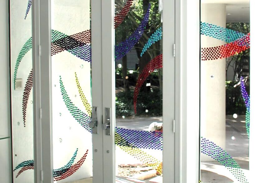 Glass doors with colorful dot patterns creating wave designs, letting natural light into a modern interior space.