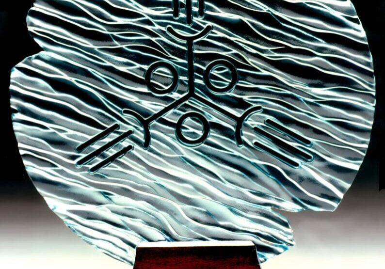 Sculptural award with abstract silver patterns and symbols on a wooden base.