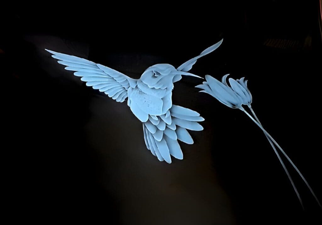 A paper art installation featuring a blue bird in flight approaching a flower, displayed against a dark background.