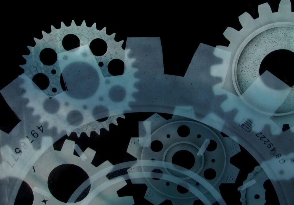 A monochrome image of overlapping gears and cogwheels with a translucent effect.